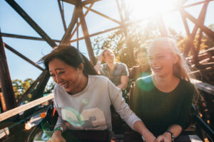 Young people on a thrilling roller coaster ride at amusement park. Group of friends having fun at fair.